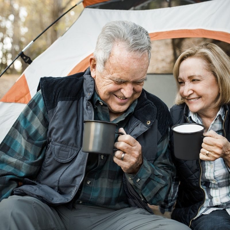 Happy elderly couple having coffee by the tent in the forest